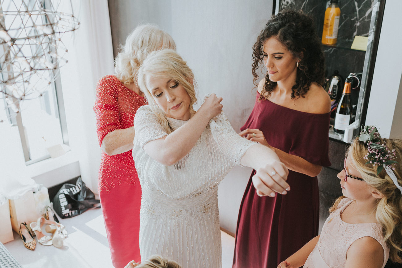 Bridesmaids helping the bride fitting into her wedding dress.