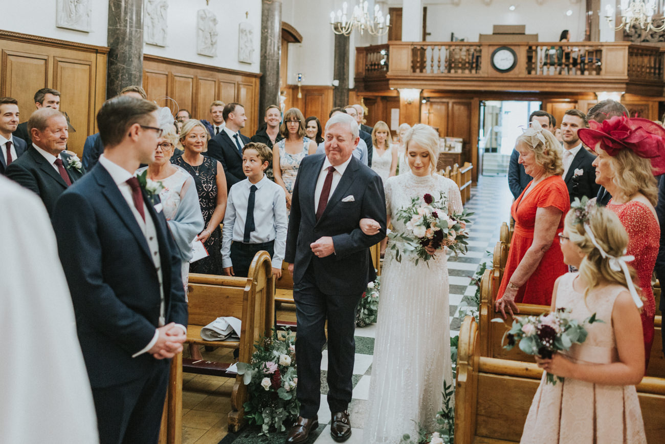 Dad and Bride walking the aisle at London St Mary Moorfields Church. Dad winks to the groom.