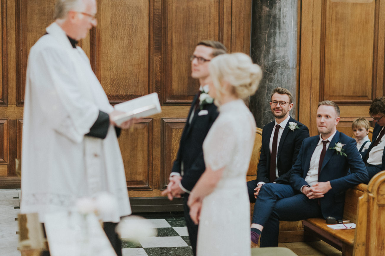 Best man watch the bride and groom during their wedding ceremony at St Mary Moorfields Church London.