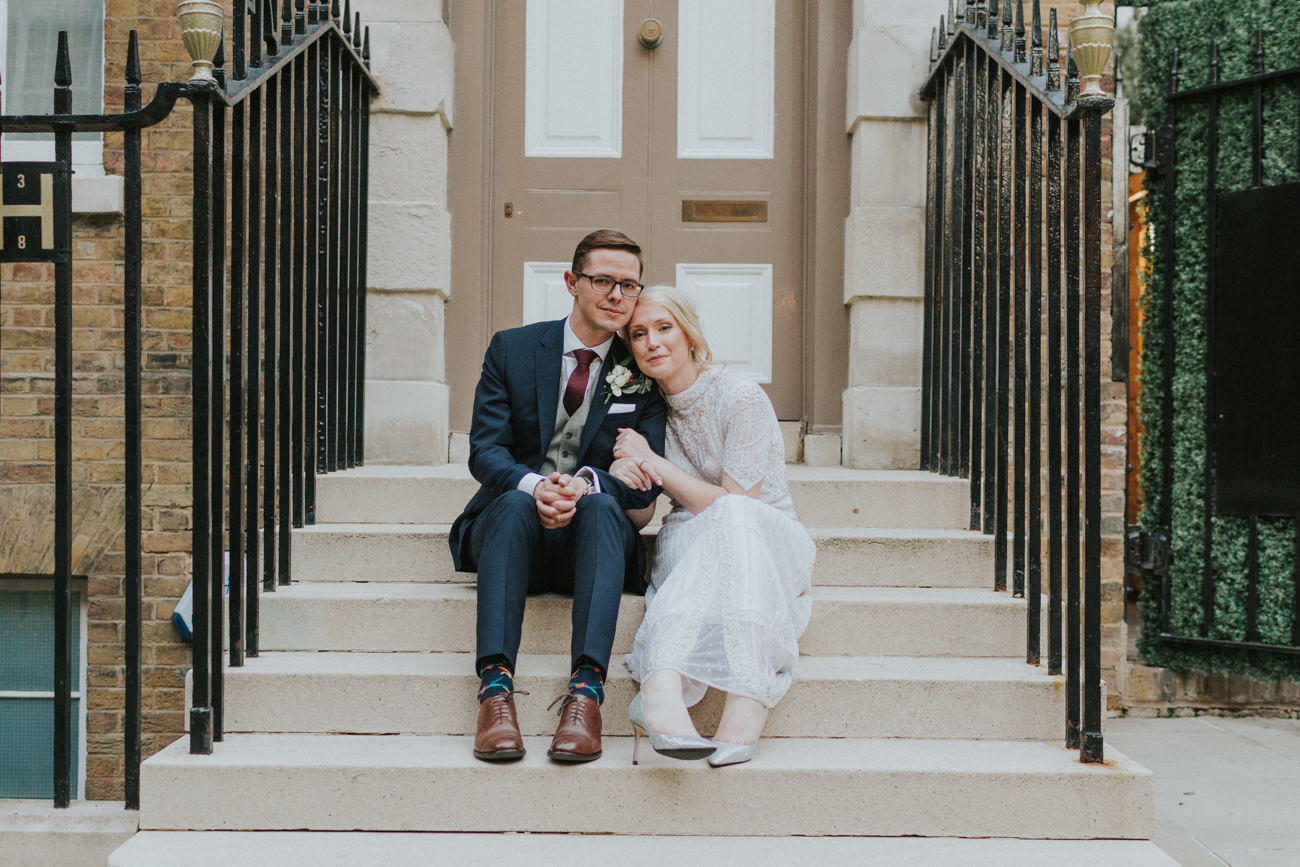 Bride and groom in front of a door in London. They are sitting on the steps looking into the camera.

