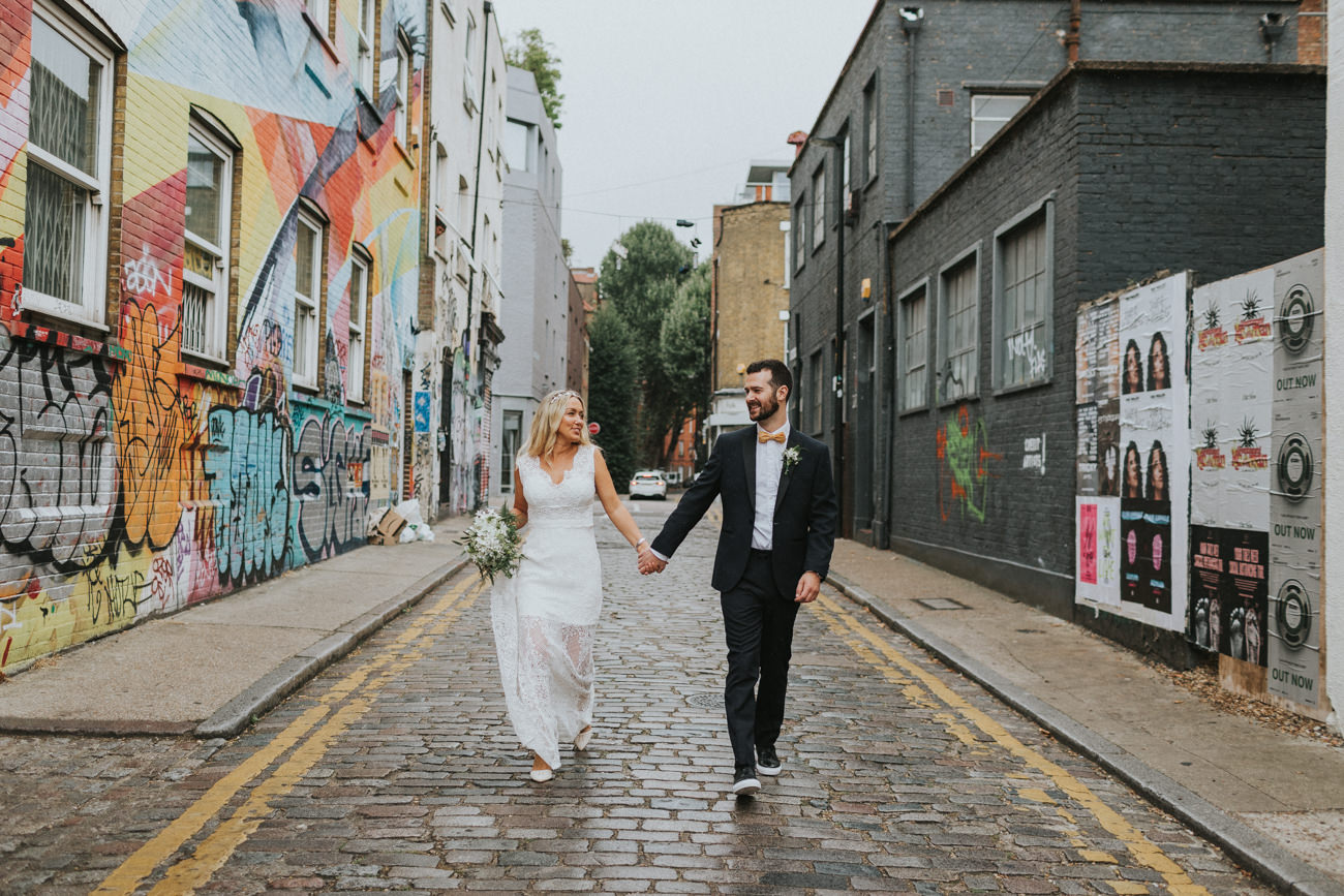 Couple running through the streets_ London Micro Wedding Hackney Town Hall Bride and groom Portraits in arty Shoreditch Alternative Wedding Photographer We Heart Pictures