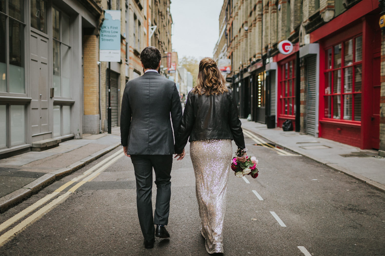 Bride and groom holding hands and walking away in Shoreditch London.