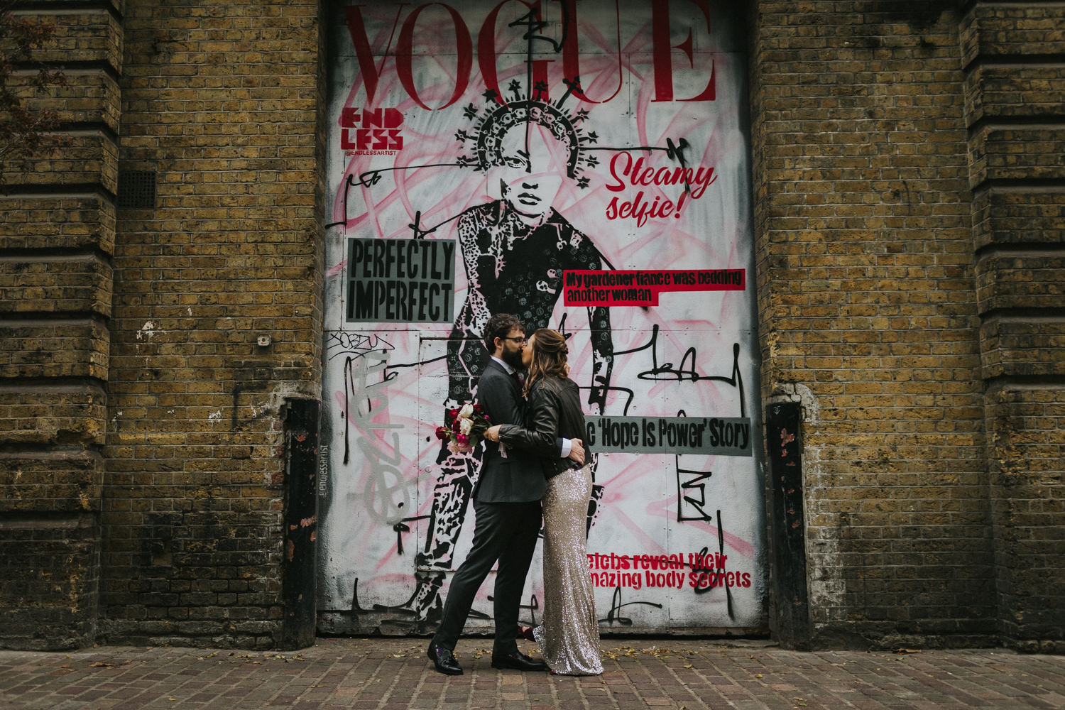 Newlyweds kissing in the streets of London in front of street art.