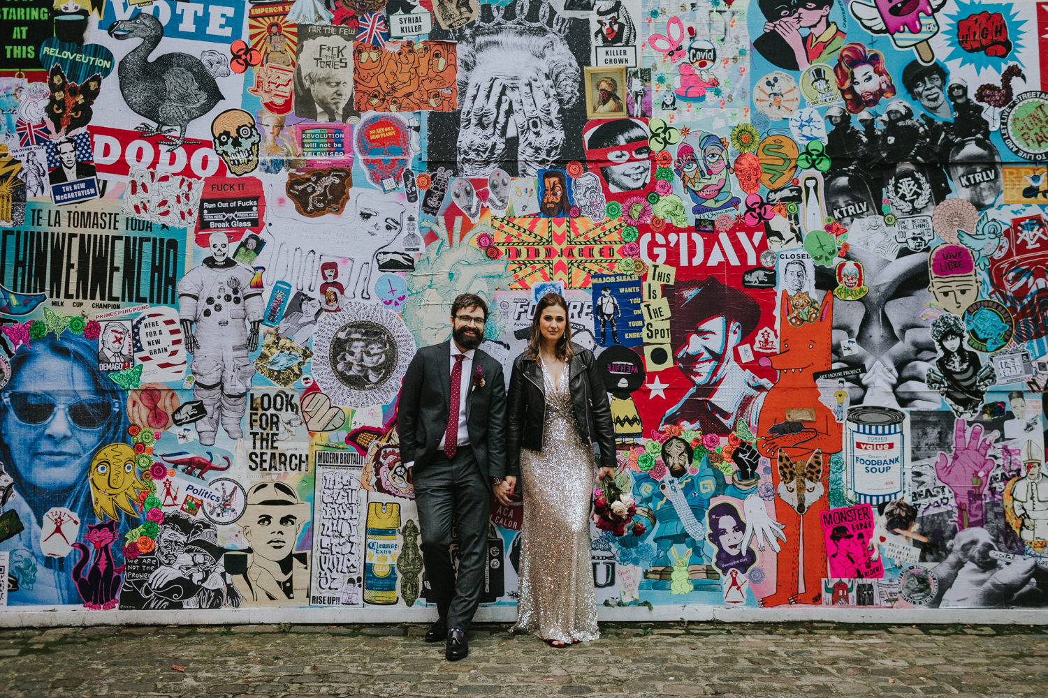 Bride and groom holding hands in front of a wall with street art in Shoreditch London.