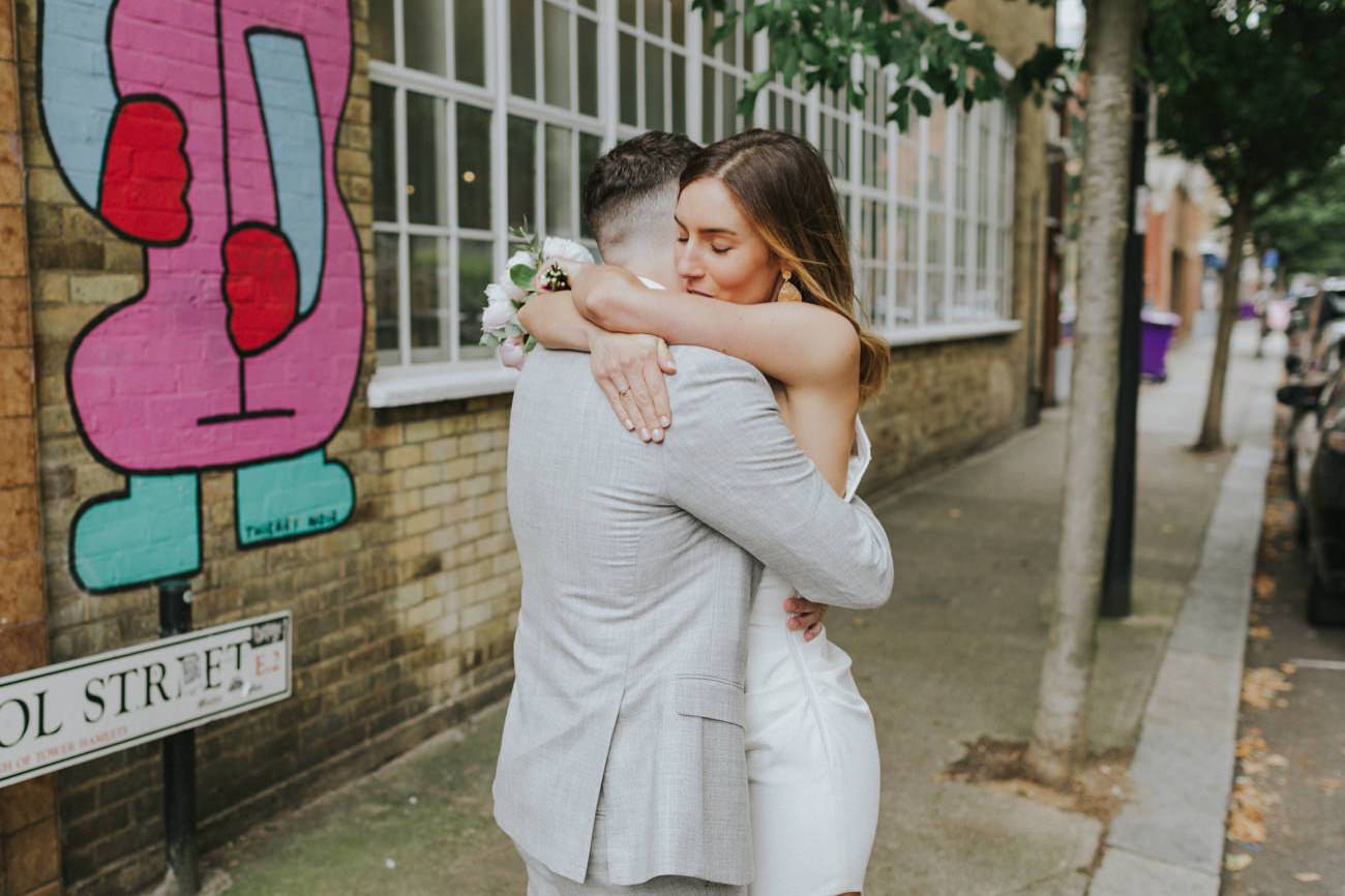 Bride and Groom hugging in front of street art in Shoreditch, London.  