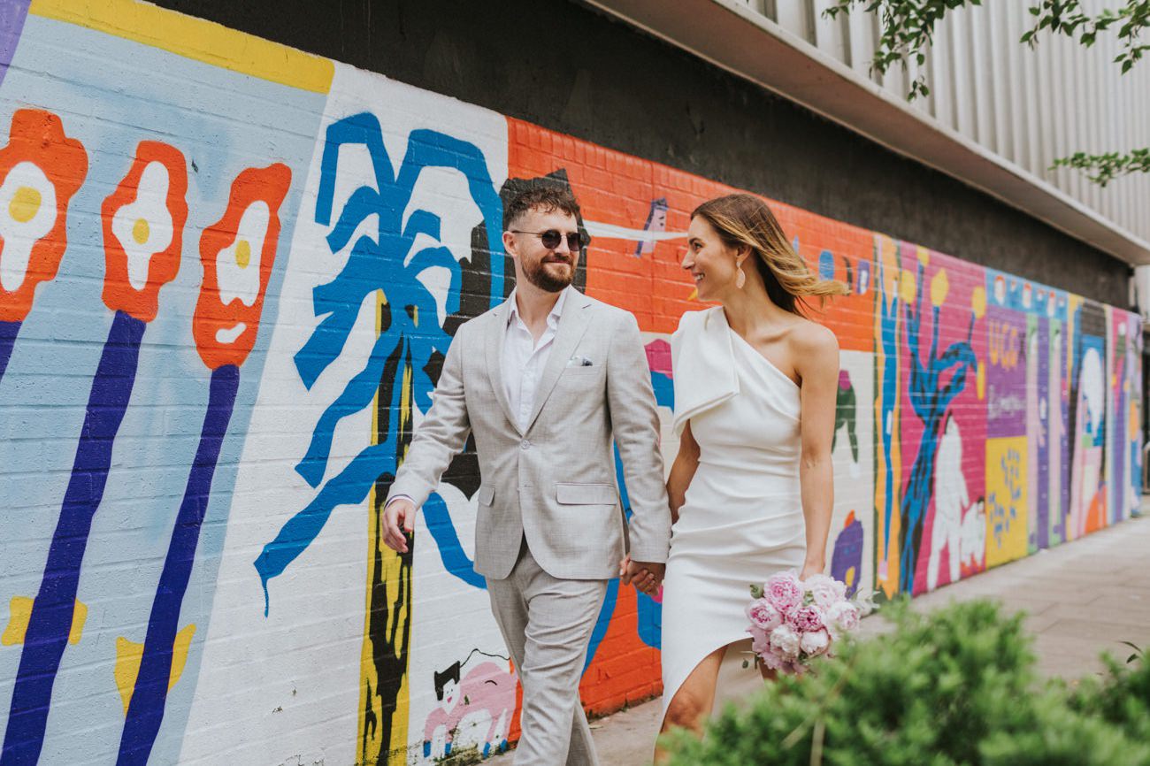Bride and Groom walking happy in front of street art in Shoreditch London.