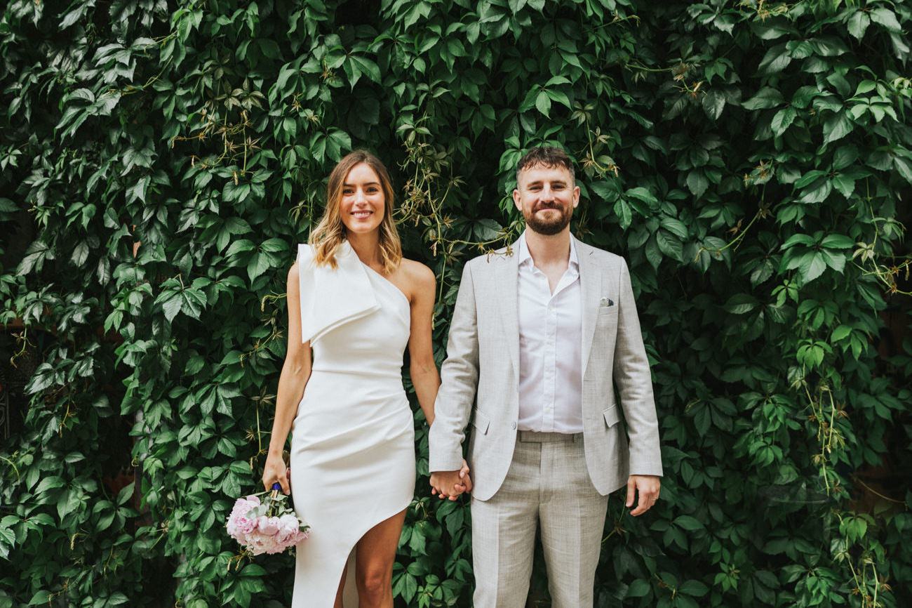 Bride and groom in front of a leafy wall in London.