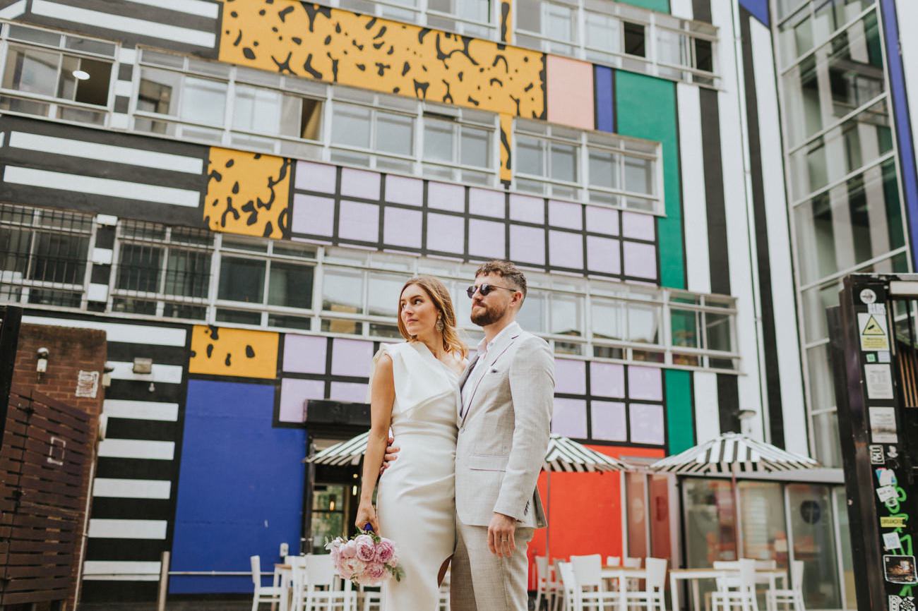 Bride and Groom gazing, in front of street art by Camille Wall, in Shoreditch London.