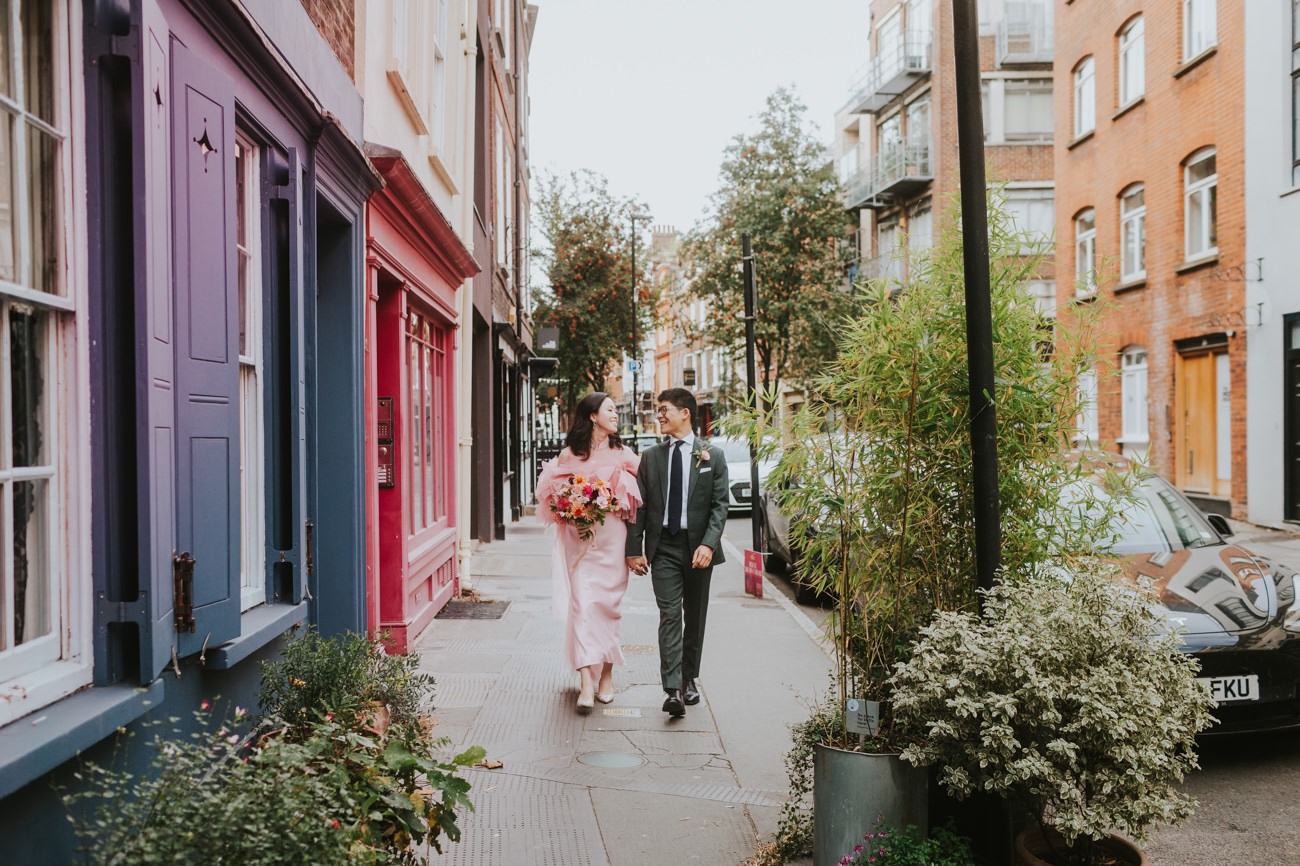A bride and groom walk down a colourful London Street